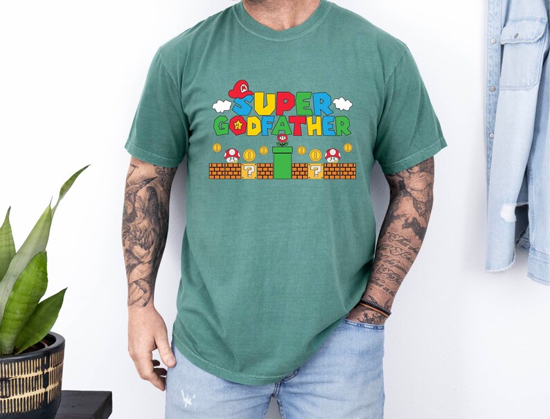 Puede incluir: Una camiseta verde con un gr&aacute;fico de un personaje de Super Mario Bros. sosteniendo una flor y el texto "SUPER GODFATHER".