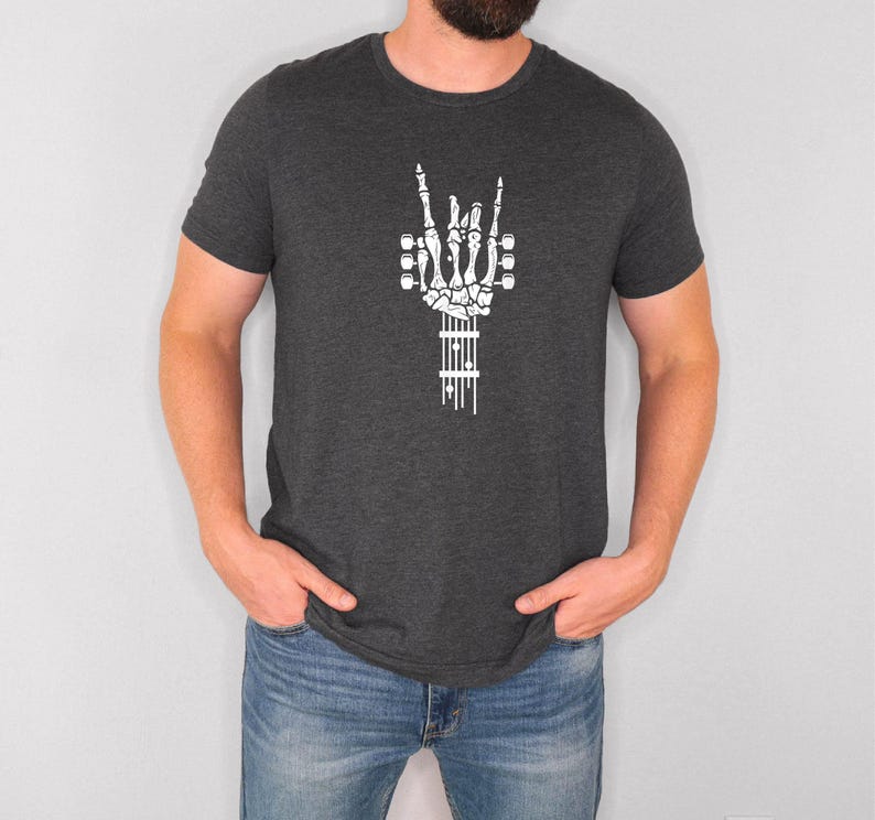Pu&ograve; includere: Una t-shirt grigio scuro melange con una mano scheletrica bianca che fa il segno rock and roll, tenendo una chitarra. La chitarra &egrave; fatta di ossa e ha un contorno bianco.
