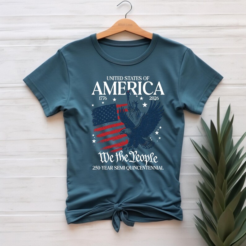 May include: Teal t-shirt with a patriotic design. The graphic includes the text "UNITED STATES OF AMERICA 1776-2026" above a stylized American flag and a soaring eagle. Below, it reads "We the People" and "250-YEAR SEMI-QUINCENTENNIAL."