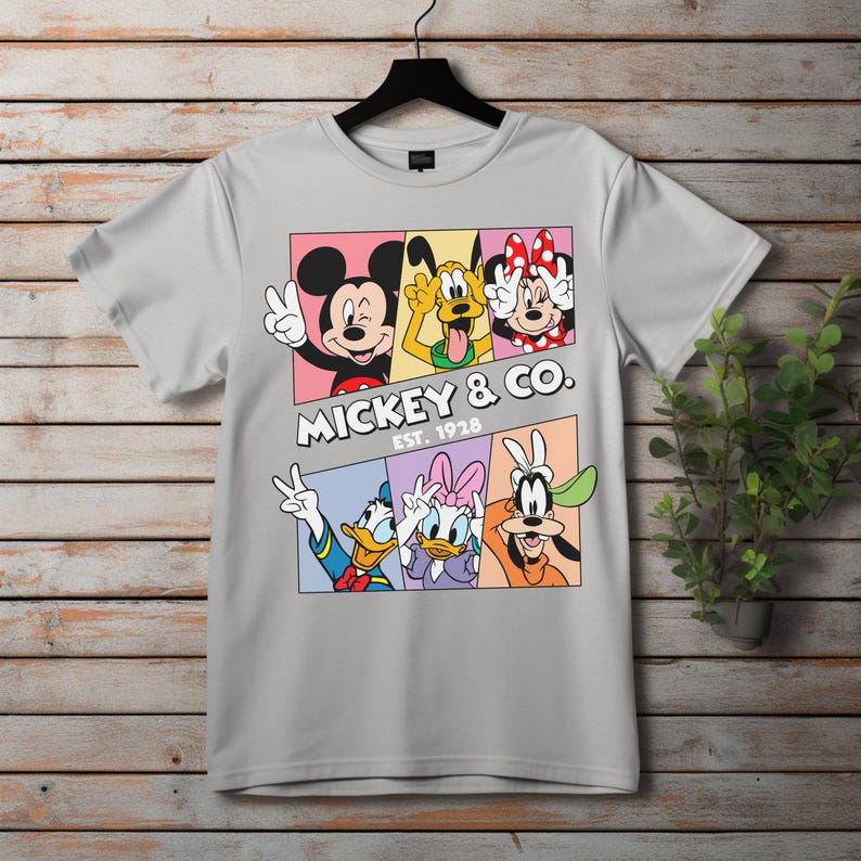 Puede incluir: Camiseta gris claro con un dise&ntilde;o colorido de Mickey Mouse, Pluto, Minnie Mouse, Donald Duck, Daisy Duck y Goofy. El texto "Mickey & Co. Est. 1928" tambi&eacute;n est&aacute; impreso en la camiseta.