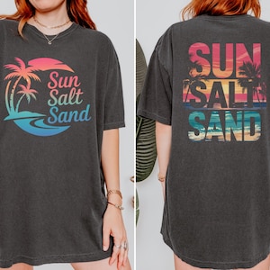 K&ouml;nnte beinhalten: Dunkelgraues T-Shirt mit einem farbenfrohen Grafikdesign eines Sonnenuntergangs, Palmen und den Worten "Sun Salt Sand". Das Design wiederholt sich auf der R&uuml;ckseite. Das Shirt hat kurze &Auml;rmel und eine lockere Passform.
