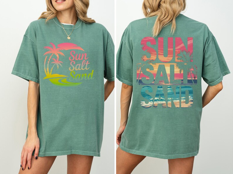 K&ouml;nnte beinhalten: Ein gr&uuml;nes T-Shirt mit den Worten "Sun Salt Sand" in einem farbenfrohen Farbverlauf. Auf der Vorderseite des T-Shirts befinden sich Palmen und ein Sonnenuntergangsdesign. Auf der R&uuml;ckseite des Shirts stehen ebenfalls die Worte "Sun Salt Sand" mit Sonnenuntergang und Palmen.