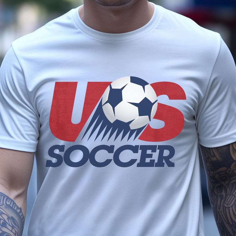 May include: A white short-sleeved t-shirt featuring a graphic design with the red letters US, a black and white soccer ball replacing the letter O, and the word SOCCER printed in dark blue capital letters underneath the graphic.
