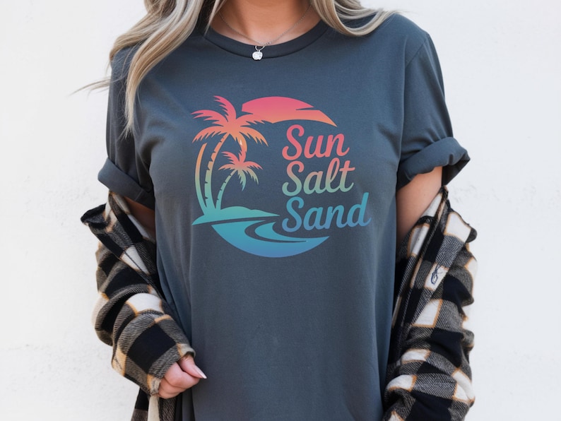 K&ouml;nnte beinhalten: Dunkelgraues T-Shirt mit einer farbenfrohen Grafik von Palmen, einer Sonne und den Worten "Sun Salt Sand". Das Design weist einen Farbverlauf aus Pink, Orange, Blau und Gr&uuml;n auf. Das Shirt hat hochgekrempelte &Auml;rmel.