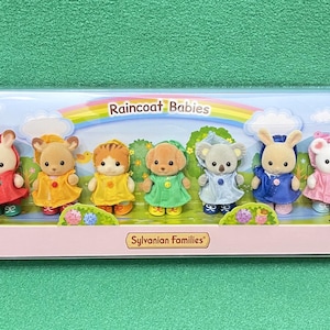 May include: A boxed set of Sylvanian Families Raincoat Babies. The set includes six animal figures wearing colorful raincoats. The packaging features a rainbow, clouds, and the text "Raincoat Babies" and "Sylvanian Families".