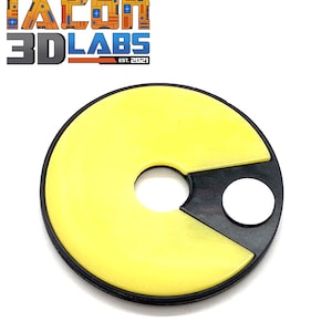 Puede incluir: Un llavero con forma de Pac-Man amarillo y negro. El llavero está hecho de plástico y tiene un borde negro.