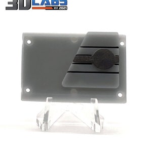 May include: A gray plastic wall panel with a black and gray stripe design. The panel has two small holes on the top and bottom edges. The panel is on a clear plastic stand.