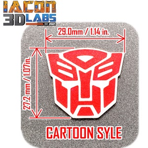 May include: Red cartoon-style Transformers logo with white outlines. The logo is 27.2 mm tall and 29.0 mm wide. The logo is on a grey textured background.
