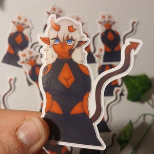 May include: A sticker featuring a cartoon character with orange skin, white hair, and blue eyes. The character has horns and a tail, and is wearing a black outfit with orange accents. Several stickers are visible in the image.