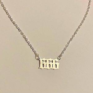 May include: A silver necklace with a fine chain. The pendant displays the number "666" in a gothic font. The necklace is shown against a plain background.