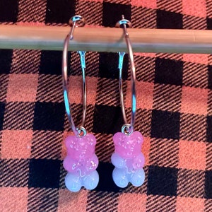 May include: A pair of silver hoop earrings with pink and white gummy bear charms.