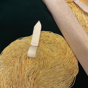 May include: A large spool of gold-colored cord or string. The cord is wound tightly and is ready to be used for crafting or other projects.