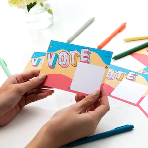 May include: Four colorful cards with the word "VOTE" in large, 3D letters. The cards have a blue, yellow, and pink background with white space for writing.