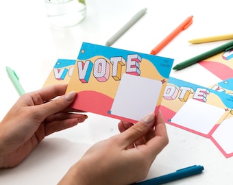 Può includere: Quattro carte colorate con la parola "VOTE" in grandi lettere 3D. Le carte hanno uno sfondo blu, giallo e rosa con spazio bianco per scrivere.
