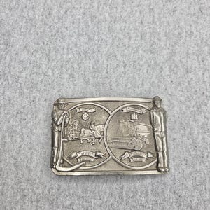Peut inclure: Une boucle de ceinture rectangulaire en métal argenté présentant deux scènes circulaires en relief. Le côté gauche montre une personne avec une faux et une moissonneuse tirée par des chevaux avec le texte McCormick Reaper 1831. Le côté droit montre une moissonneuse-batteuse avec le texte Axial-Flow Combine 1977-1981.