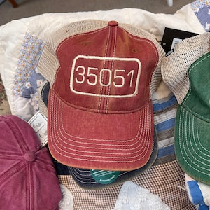 May include: A red and beige mesh baseball cap with the number "35051" embroidered on the front. The cap has a white stitched brim and a brown leather strap.