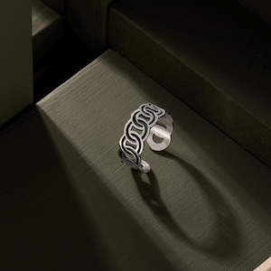 May include: A silver ring with a chain-like design. The ring is on a green surface.
