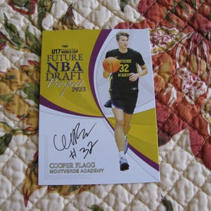 Puede incluir: Una tarjeta de baloncesto con Cooper Flagg, un futuro prospecto del draft de la NBA. La tarjeta tiene un diseño amarillo y morado con el texto "U17 World Cup" y "2023". Flagg aparece con una camiseta negra con el número 32.
