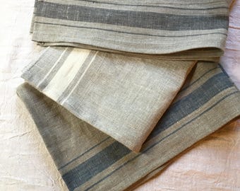 May include: Three linen tea towels with different colored stripes. The top towel has gray stripes, the middle towel has white stripes, and the bottom towel has blue stripes.