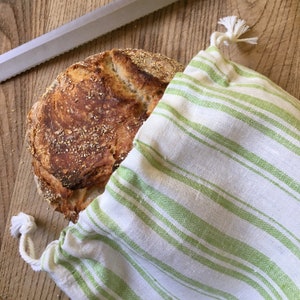 May include: A freshly baked loaf of bread in a white and green striped cloth bag. The bread has a golden brown crust and is slightly cracked on top.