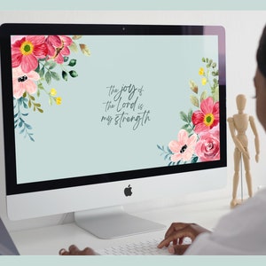 May include: A computer screen displaying a floral desktop wallpaper with the text "the joy of the Lord is my strength". The screen is on a white desk with a person's hand typing on a keyboard.