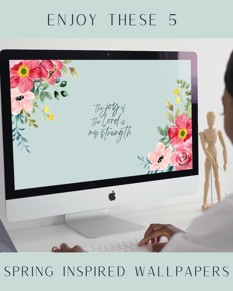 May include: A computer screen displaying a floral desktop wallpaper with the text "the joy of the Lord is my strength". The screen is on a white desk with a person's hand typing on a keyboard.