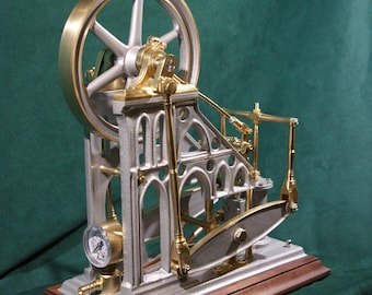 May include: A small, silver and gold model steam engine with a wooden base. The engine features a flywheel, a pressure gauge, and a complex system of gears and levers.