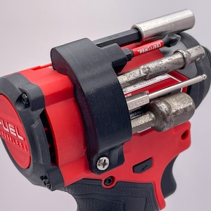 May include: A red and black power drill with a black 3D printed attachment holding various bits and a screwdriver. The drill has the text "FUEL" on the side.