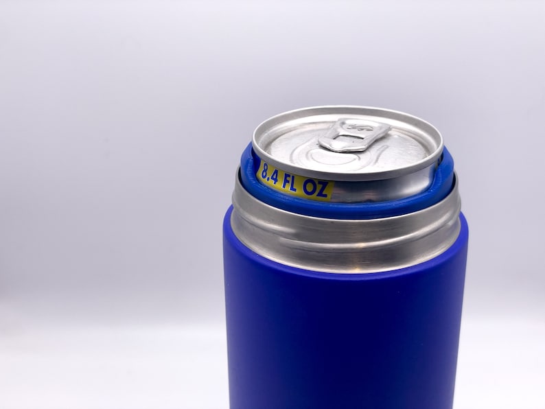 May include: A blue and silver can cooler with a stainless steel liner. The cooler has a blue silicone sleeve and a silver lid. The can cooler is designed to hold a 8.4 fl oz can.