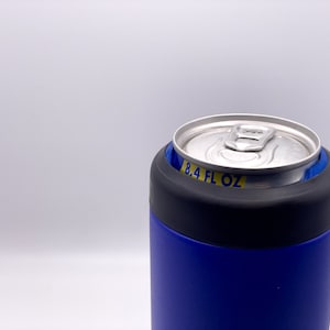 May include: A blue and black insulated can holder with a silver can inside. The can has a yellow label that reads "8.4 FL OZ".