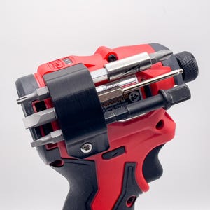 May include: A red and black power drill with a black bit holder containing various metal drill bits. The drill has a black handle and a black bit holder. The drill bits are silver and black.