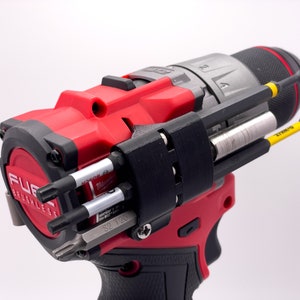 May include: A red and black cordless drill with a black accessory holder attached to the side. The holder has several different drill bits and screwdriver bits attached to it. The drill has the words "FUEL" and "BRUSHLESS" printed on the side.