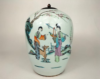 Puede incluir: Un jarrón de porcelana blanca con tapa, decorado con una escena pintada a mano de dos mujeres y un ciervo en un jardín. Las mujeres visten túnicas coloridas y el ciervo es marrón con manchas blancas. El jarrón tiene un delicado diseño floral alrededor del borde.