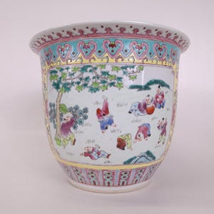 Pode incluir: Um grande vaso de cerâmica com fundo branco e uma cena colorida de crianças a brincar ao ar livre. A borda e a base são decoradas com padrões em rosa, azul e amarelo. A ilustração central mostra figuras em várias posições.