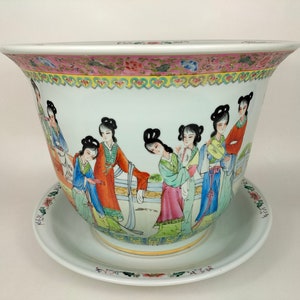 Könnte beinhalten: Ein weißer Porzellan-Pflanztopf mit Untersetzer, der mit einem handgemalten Design von Frauen in traditioneller chinesischer Kleidung verziert ist. Der Topf hat eine breite, runde Öffnung und einen gewellten Rand. Der Untersetzer hat einen floralen Rand.
