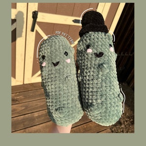 Könnte beinhalten: Zwei grüne, gehäkelte Plüschtiere in Form von Gurken. Eine Gurke trägt einen schwarzen, gehäkelten Hut. Die Gurken haben gestickte Gesichter mit lächelnden Ausdrücken. Der Text "PDF PATTERN" ist im Bild sichtbar.