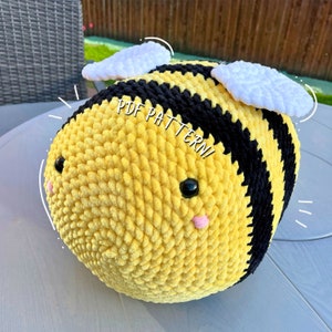 May include: A crocheted bee plush toy with black and yellow stripes, white wings, and pink cheeks. The bee has a text overlay that says "PDF PATTERN!"