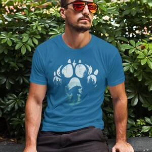 Op de afbeelding: Een tealkleurig t-shirt met een wit berenpootafdrukontwerp met een berensilhouet en bomen. Dit grafische t-shirt is gemaakt van een zacht materiaal en is geschikt voor vrijetijdskleding.