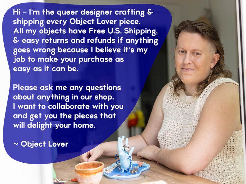 May include: A person sitting at a table with a blue ceramic hand ring holder. The ring holder is filled with rings and a blue beaded necklace. The person is wearing a white crocheted top. The text "Hi - I'm the queer designer crafting & shipping every Object Lover piece. All my objects have Free U.S. Shipping, & easy returns and refunds if anything goes wrong because I believe it's my job to make your purchase as easy as it can be. Please ask me any questions about anything in our shop. I want to collaborate with you and get you the pieces that will delight your home. ~ Object Lover" is visible in the image.