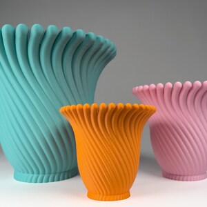 May include: Three ceramic vases in different sizes and colors. The largest vase is teal blue, the medium vase is orange, and the smallest vase is pink. All three vases have a unique, swirling, textured design.