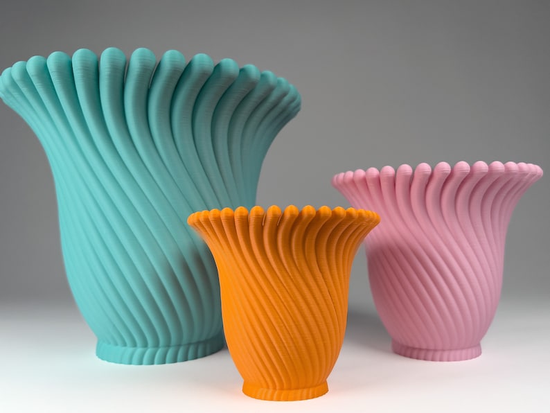May include: Three ceramic vases in different sizes and colors. The largest vase is teal blue, the medium vase is orange, and the smallest vase is pink. All three vases have a unique, swirling, textured design.