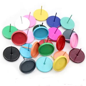 May include: A collection of colorful push pins in various shades, including pink, green, blue, and yellow. Each pin has a round head and a straight pin. The pins are scattered on a white surface.