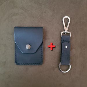 May include: A black leather cardholder with a snap closure and a matching black leather keychain with a silver carabiner clip and key ring. The items are displayed on a brown surface.