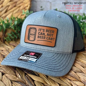 May include: Gray trucker hat with a black mesh back and a curved brim. The hat features a brown leather patch with a beer can graphic and the text "IT'S BEER CAN, NOT BEER CAN'T". The Richardson brand label is visible.