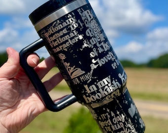 May include: Black stainless steel travel mug with a black handle. The mug has a silver design with text that reads "Emotionally attached to fictional characters. Being the person of a book. A lovely mind to be in my bookish era. It's a good day to read a book."