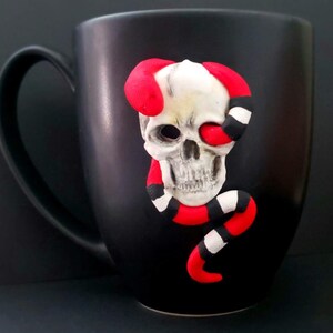 May include: Black ceramic mug with a white skull and red and white snake design.