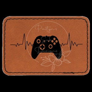 May include: A brown leather patch with a black video game controller and a heartbeat graphic. The text "Paityn's Sub Designs" is in a circle above the controller.