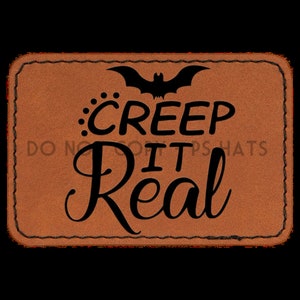 Op de afbeelding: Een bruin leren patch met een gestikte rand. De patch heeft een zwart vleermuis silhouet en de tekst "CREEP IT REAL" in een decoratief lettertype.