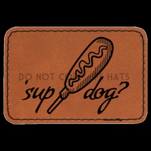 May include: A brown leather patch with a black outline and the text 'sup dog?' in a cursive font. A black and white illustration of a corn dog is in the center of the patch.