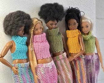 May include: Five dolls wearing crocheted tops and skirts in various colors, including blue, pink, green, yellow, and purple. The dolls have different hairstyles and skin tones.